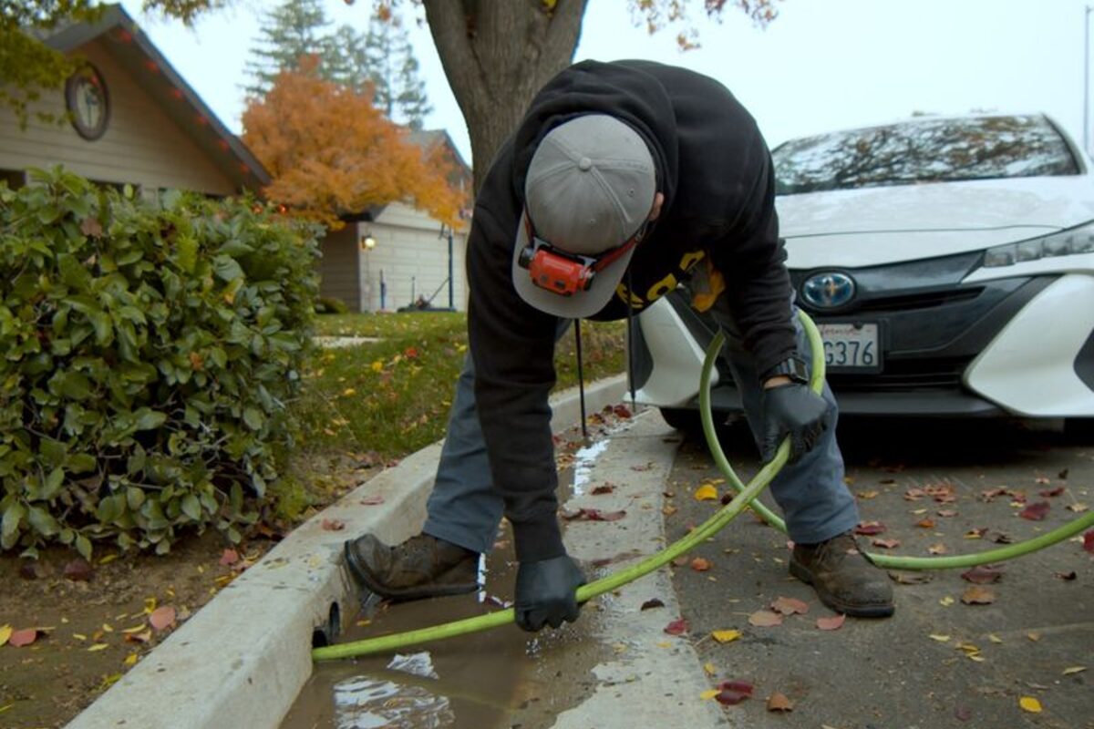 A plumber feeding a jetting hose into a line outside a house