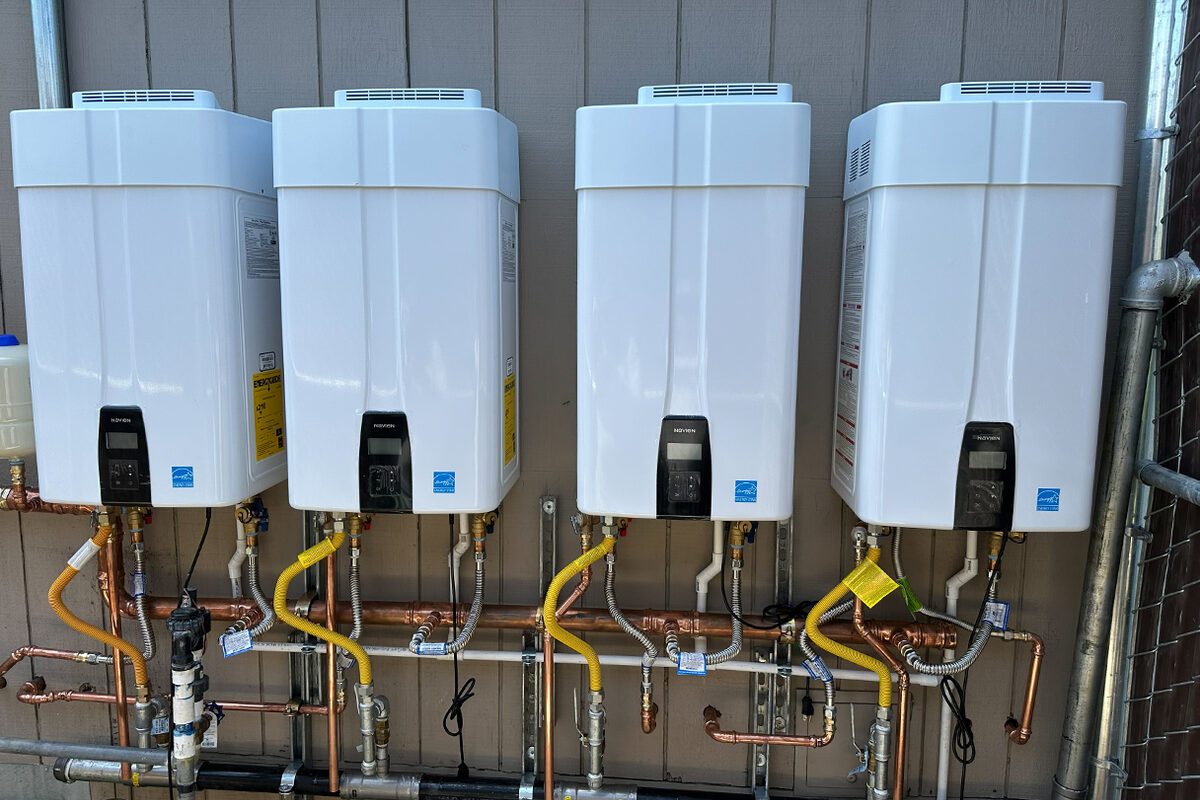 Four tankless water heaters mounted and piped on a wall